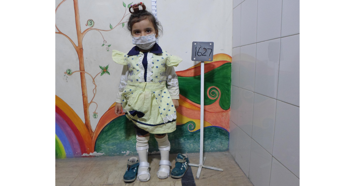 Young girl standing with a mask on, smiling and wearing new orthotic braces